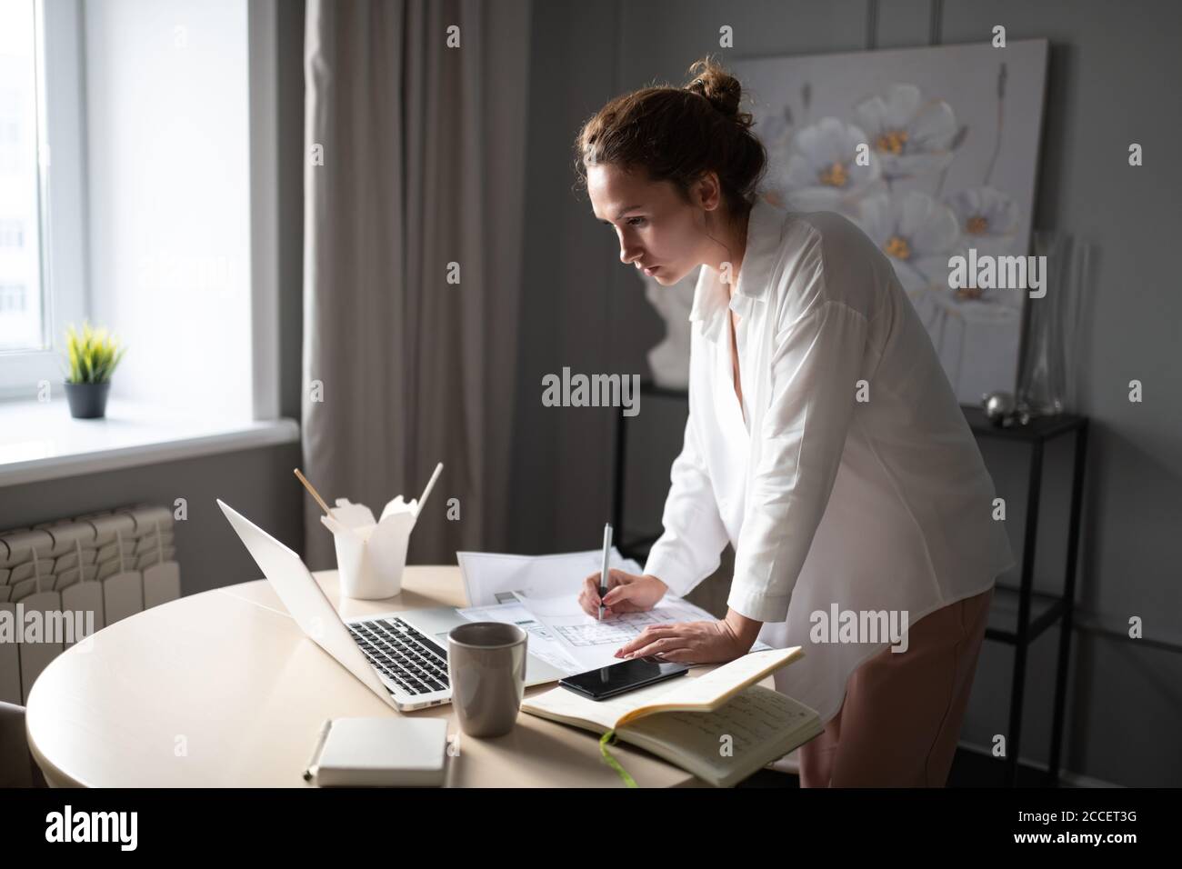 Intelligente Frau, die Daten vom Laptop auf Entwurf nach aufschreibt Mittagessen zu Hause Stockfoto