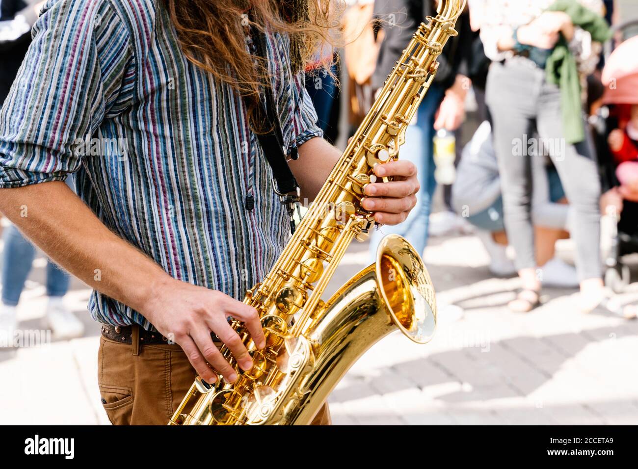 Hände eines jungen Mannes mit langen Haaren, die Saxophon spielen In einer überfüllten Straße Stockfoto