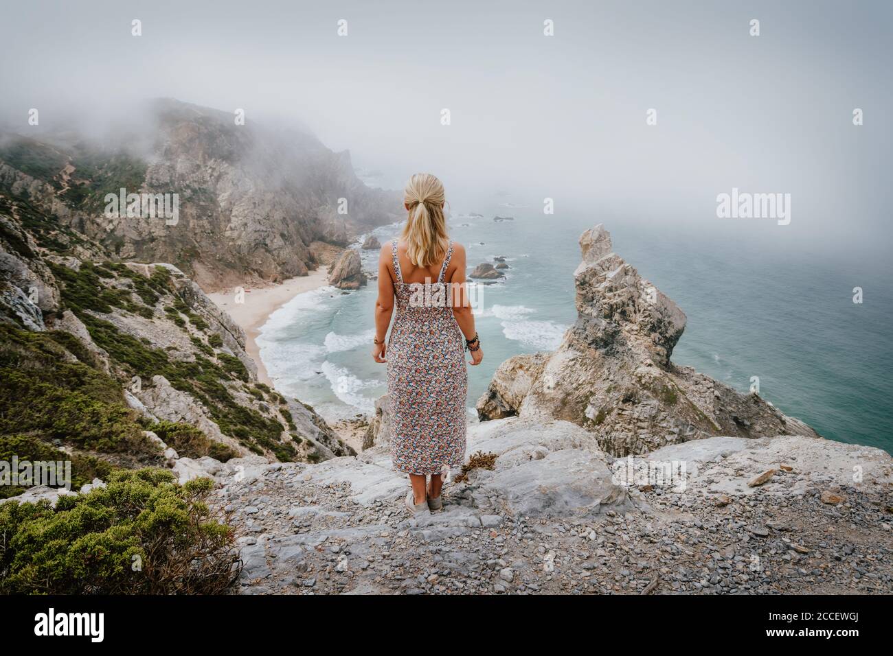 Erwachsene Frau Aufenthalt und genießen Praia da Ursa Strand am Morgen. Surreale neblige Landschaft von Sintra, Portugal. Küstenlandschaft des Atlantischen Ozeans. Stockfoto