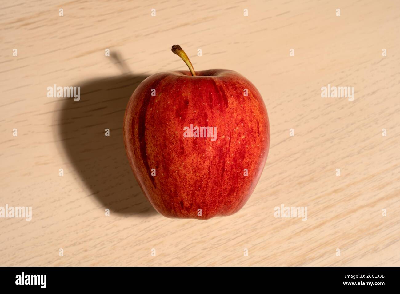 Ein Gala Apfel auf einem Holztisch mit Schatten. Stockfoto