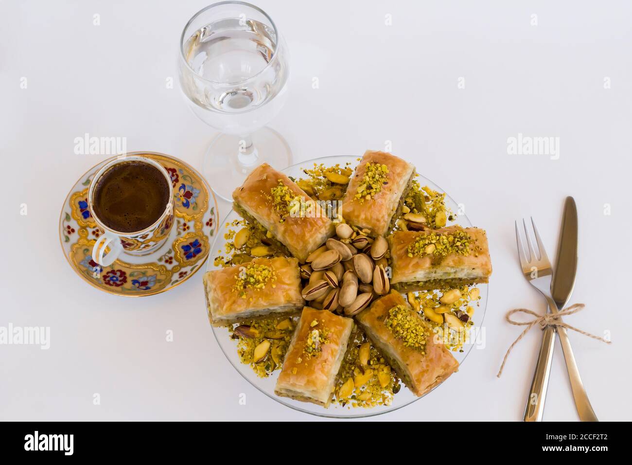 Traditionelle türkische Konditorei Dessert Pistachio Baklava auf weiß mit türkisch Kaffee, Besteck und ein Glas Wasser Stockfoto