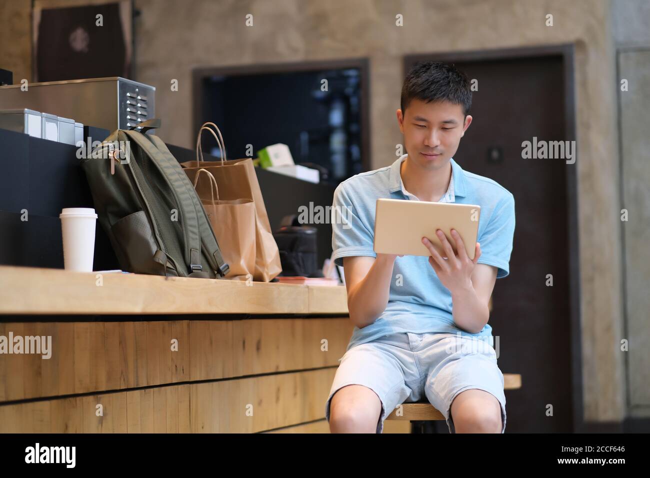 Ein hübscher asiatischer junger Mann, der im Café sitzt und Tablet-Computer benutzt. Stockfoto