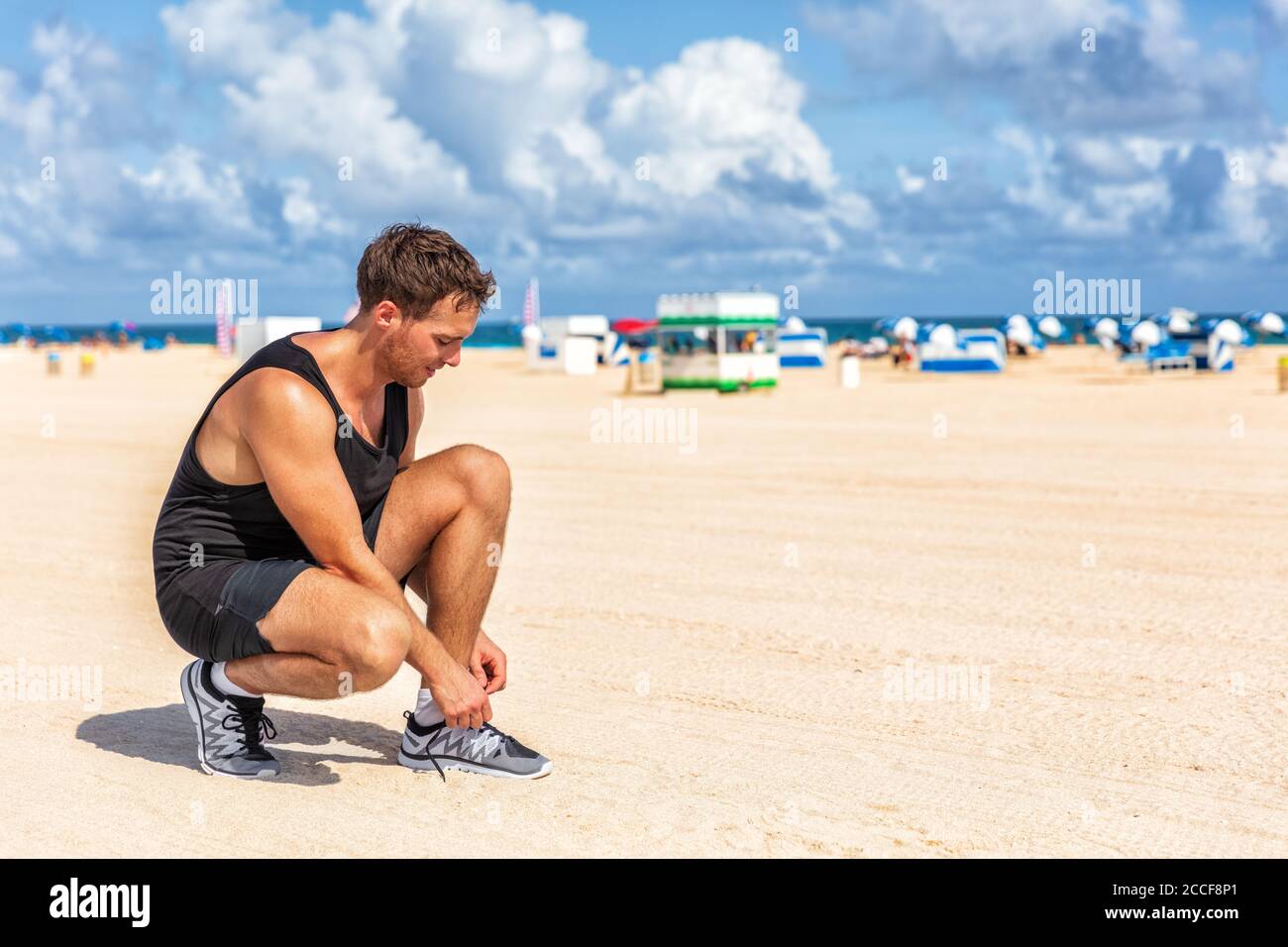Sportmann immer bereit zu laufen Binden Schnürsenkel von Laufschuhen Joggen am Strand Sand im Sommer in South Beach, Miami, Florida. Fitness-Lifestyle Stockfoto