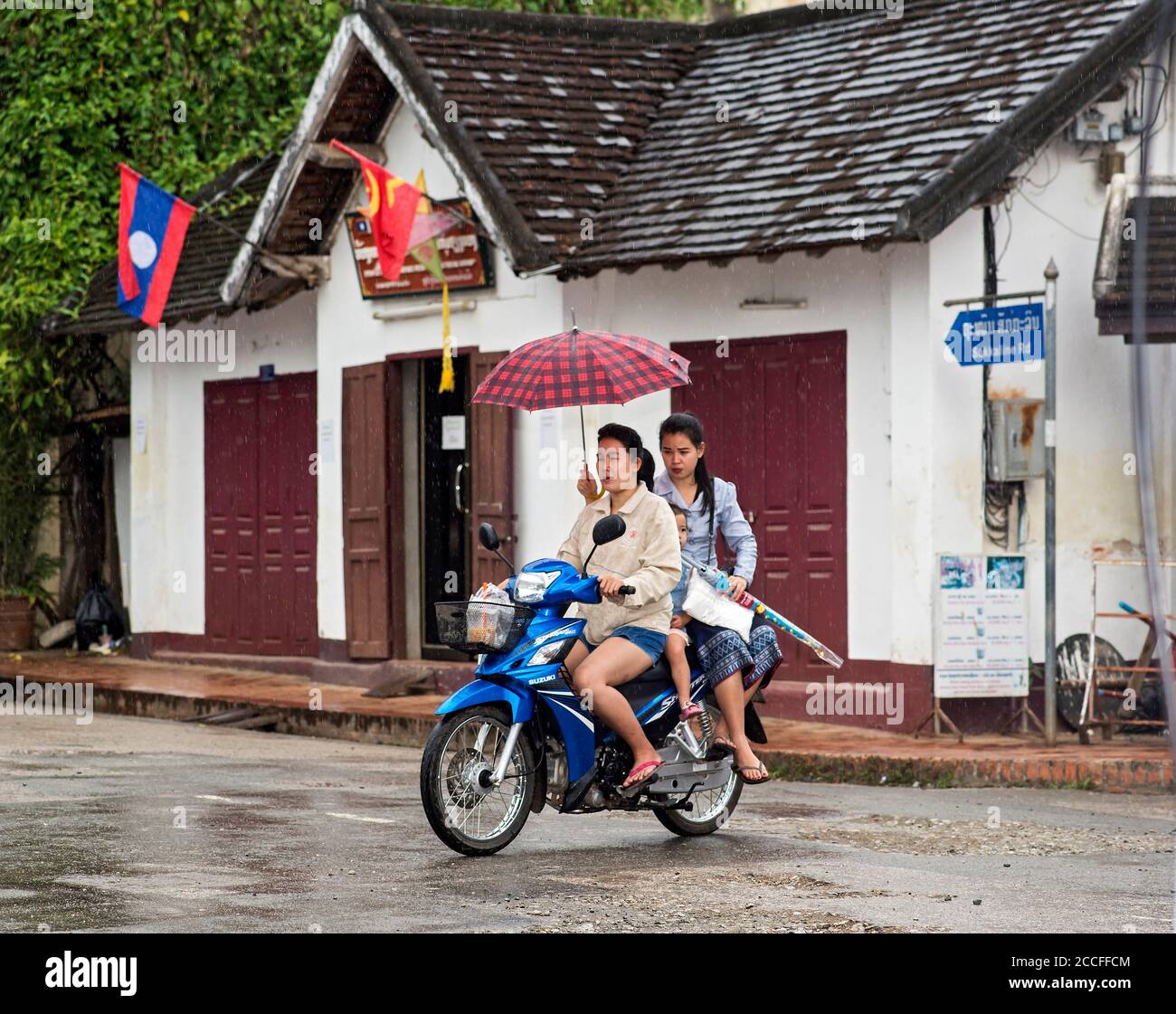 Zwei Frauen mit einem Regenschirm auf einem Moped Fahrt im Regen, Luang Prabang, Laos Stockfoto