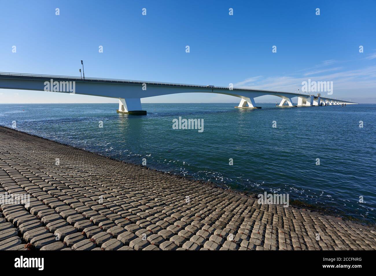 Große Zeeland-Brücke, Damm aus Steinblöcken, tiefblaues Meerwasser und wolkenloser Himmel. Niederlande, Zeeland. Stockfoto