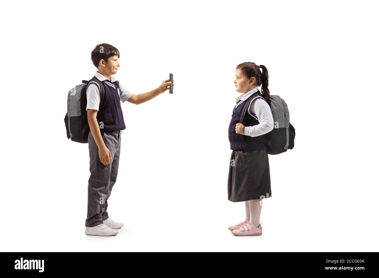 Ganzkörperaufnahme eines Schuljungen in Uniform Stehen und zeigen ein Smartphone zu einer weiblichen Schulfreundin Isoliert auf weißem Hintergrund Stockfoto