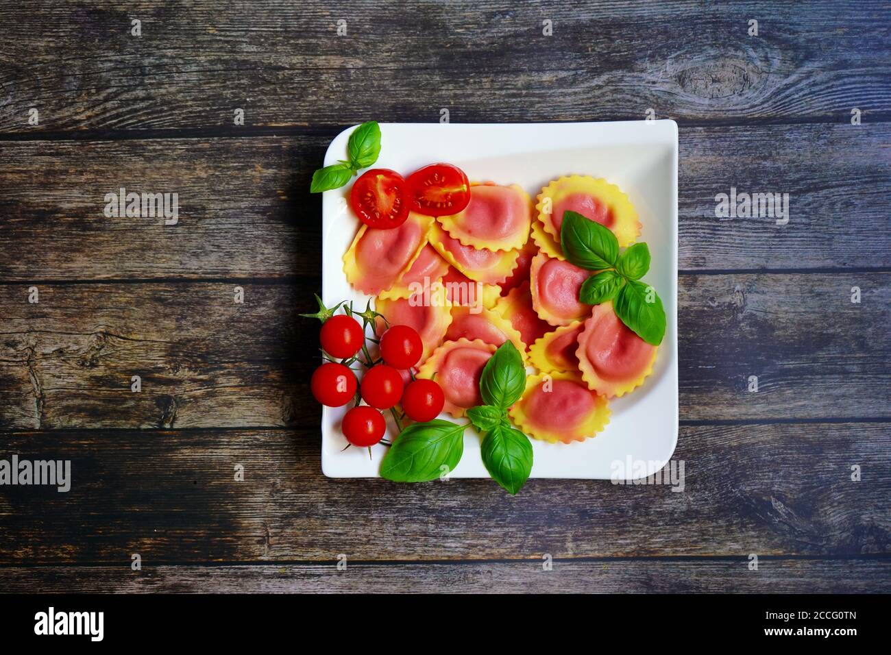 Hausgemachte Pasta / Ravioli gefüllt mit Wurzelrübe auf einem weißen Teller mit Holztisch Hintergrund. Tomaten und frisches Basilikum zur Dekoration. Stockfoto