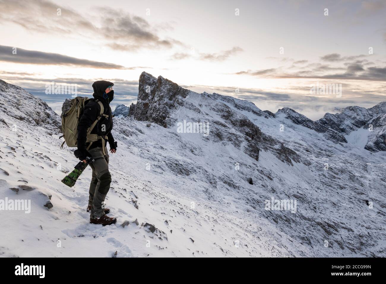 Selbstporträt Naturfotograf im Hochgebirge des Karwendels im Frühwinter, bei Schnee und Wind, mit großer Kamera und Rucksack. Stockfoto