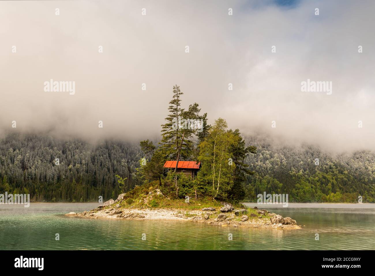 Eine kleine einsame Insel mit Blockhütte und rotem Dach, mitten im schönen Eibsee unterhalb der Zugspitze in den bayerischen Alpen des Wettersteins Stockfoto