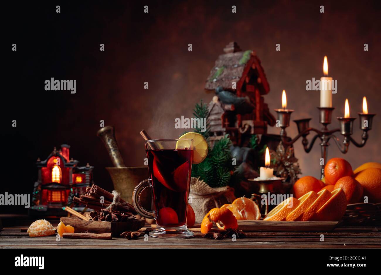 Glühwein und Weihnachtsschmuck mit Kerzenleuchtern. Auf dem Tisch verschiedene Gewürze, Zitrusfrüchte und brennende Kerzen. Stockfoto