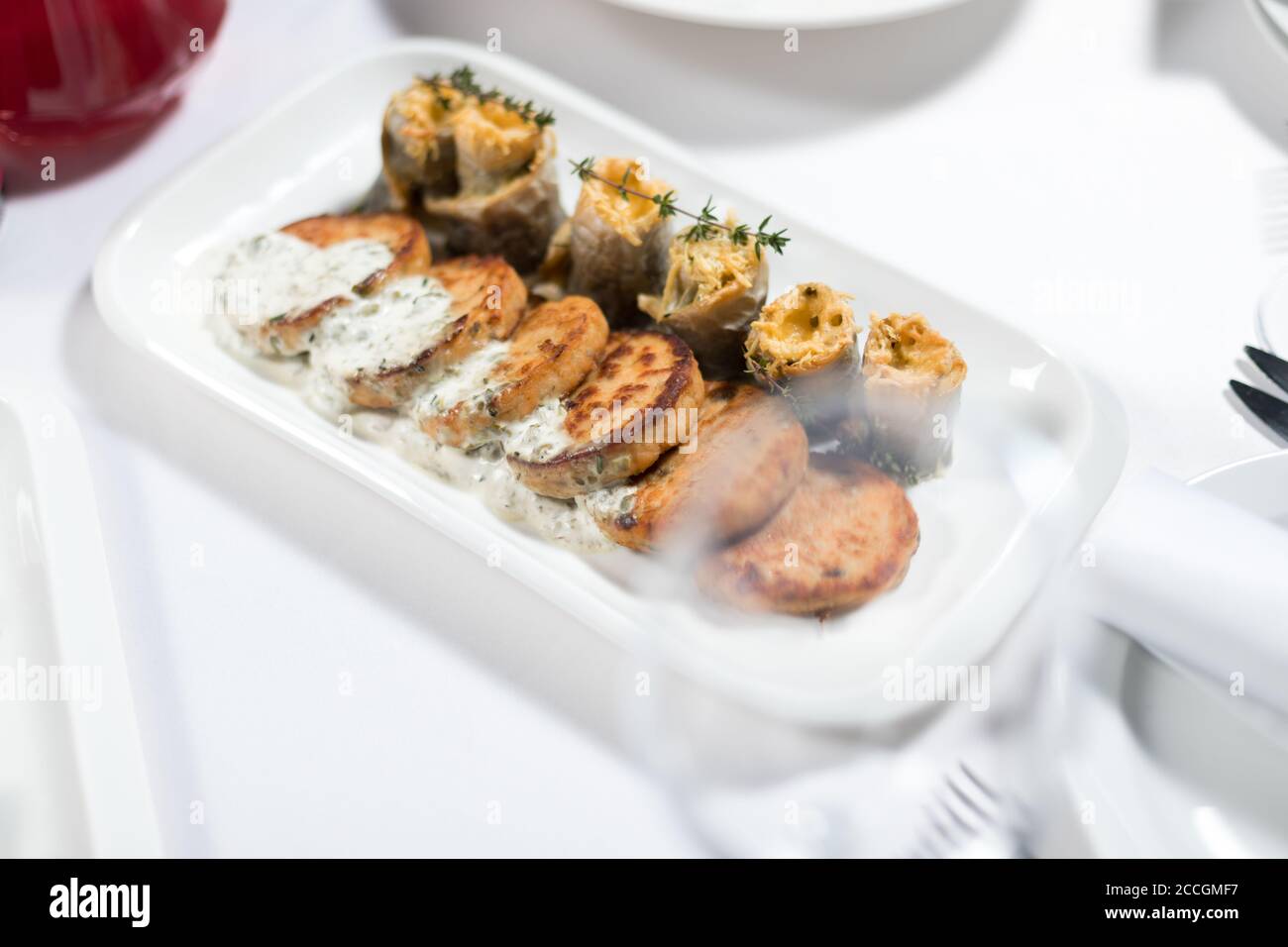 Fischkuchen mit weißer Soße und Fischfilet-Rollen, gefüllt mit Käse und Kräutern auf einem Teller auf weißem Hintergrund. Meeresfrüchte Stockfoto