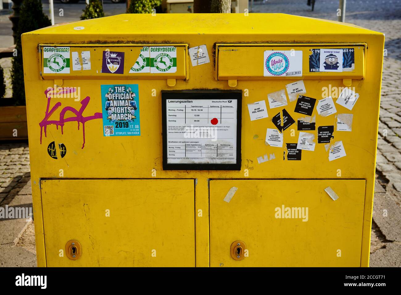 Öffentlicher gelber Briefkasten (deutsch: Briefkasten) aus Stahlplatte, teilweise mit Aufklebern bedeckt. Stockfoto