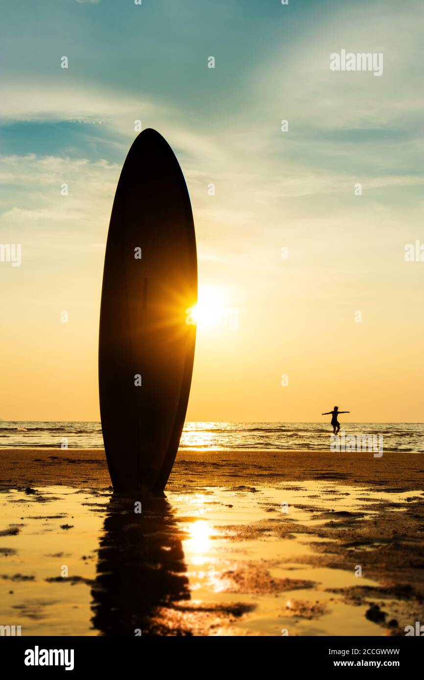Silhouette des Surf-Mannes Surfen mit einem Surfbrett am Strand bei Sonnenuntergang. Handsome Asien Mann Modell in seinen 20er Jahren. Stockfoto