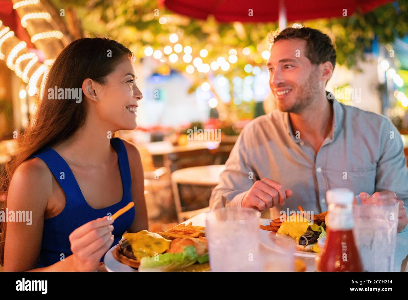 Pärchen essen Hamburger auf der Außenterrasse des Restaurants, glückliche Touristen im Sommerurlaub. Florida Reisen Menschen essen Essen in der Nacht während der Ferien Stockfoto