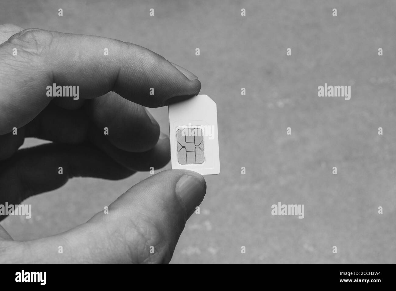 Mann hält Finger SIM-Karte auf grauem Hintergrund mit Kopierplatz, schwarz-weiß Foto Stockfoto