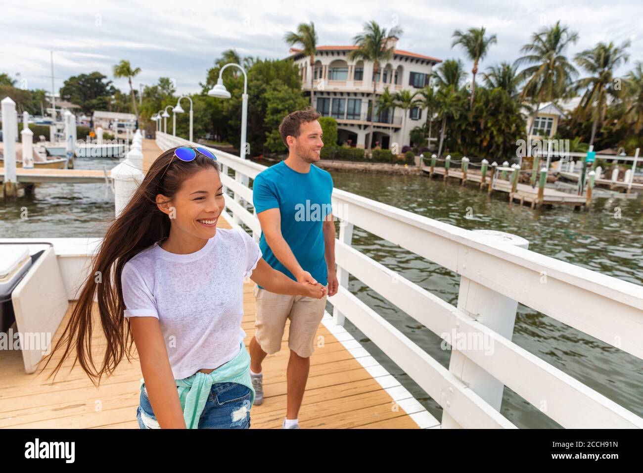 Glückliche junge casual paar Touristen zu Fuß auf Florida Promenade in Marina genießen Sommertag Hände halten. Interracial Beziehung asiatische Mädchen Stockfoto