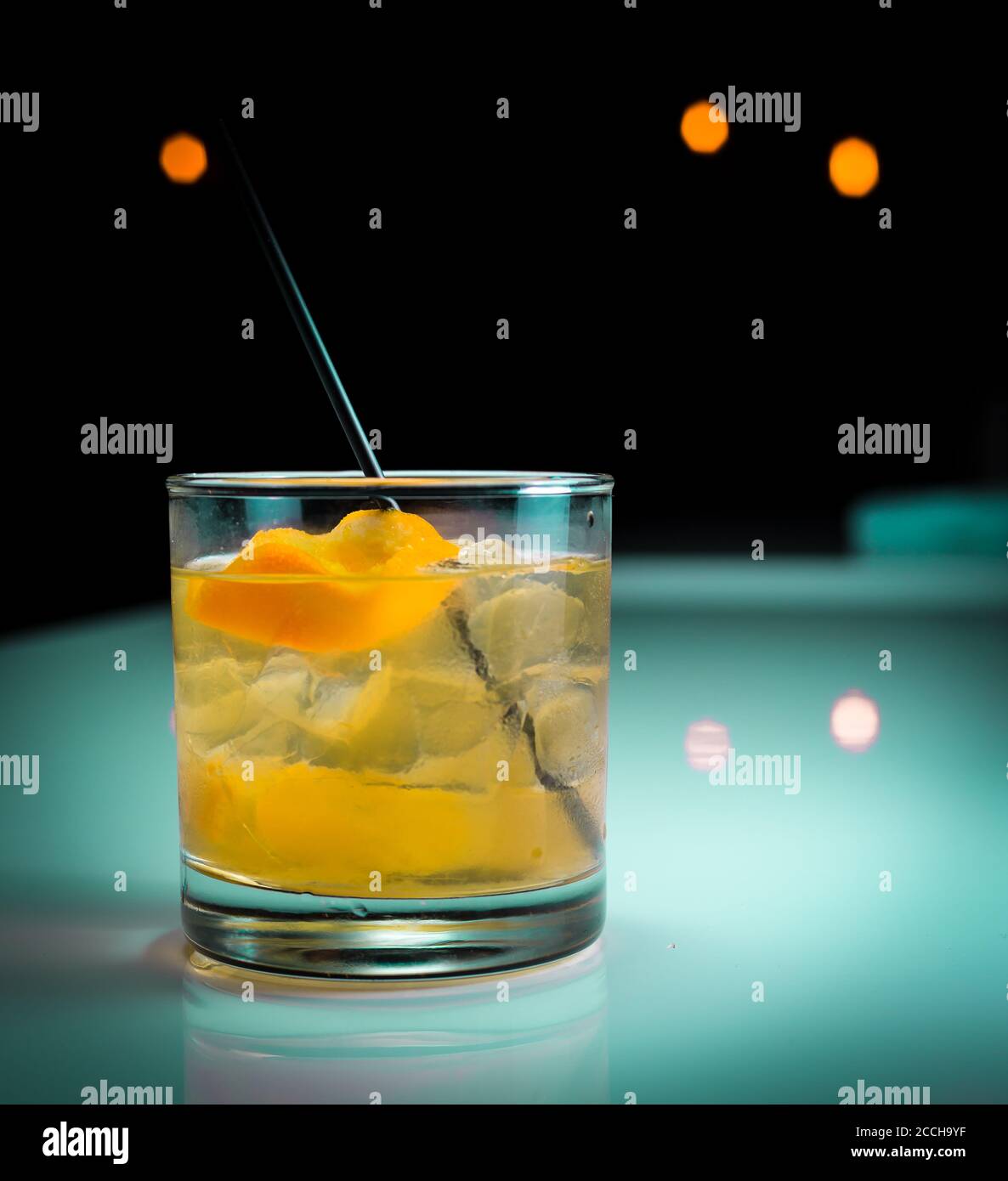 Ein erfrischender Craft-Cocktail, der auf den Felsen serviert wird, mit einer Orangenschale, die in einer modernen Bar mit türkisfarbenen Tönen zu sehen ist Stockfoto