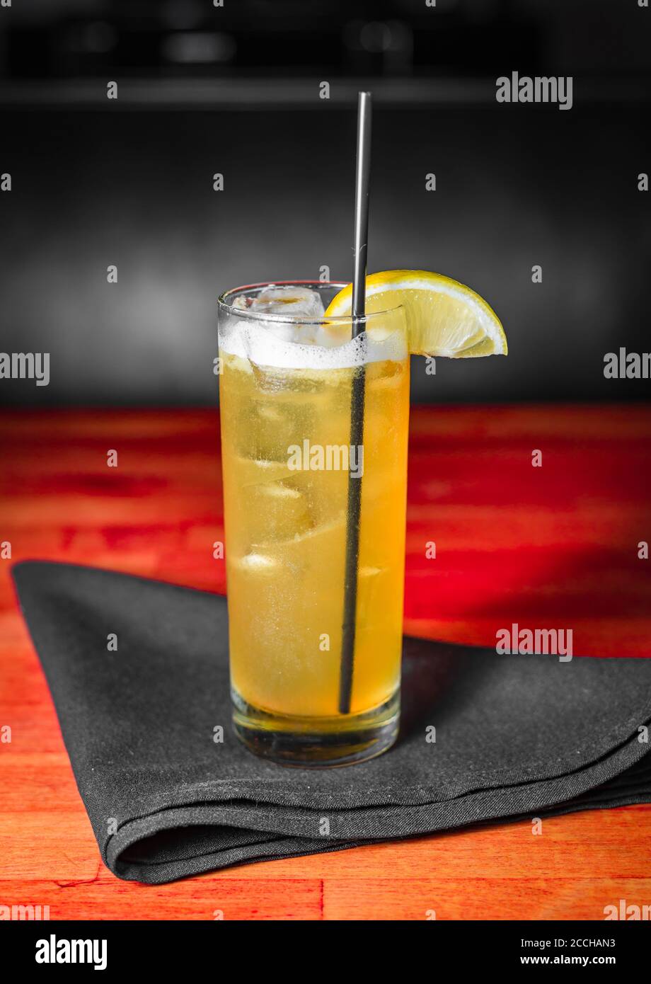 Ein gelber Craft-Cocktail in einem collins-Glas Eine schwarze Serviette auf einem rot gefärbten Holztisch Stockfoto