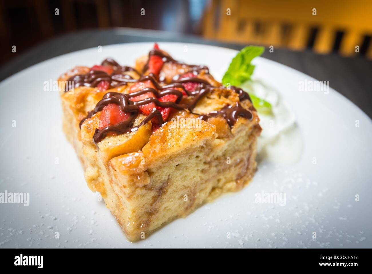 Ein weißer Teller mit einer Scheibe frisch gebackenem Brot Pudding mit Erdbeeren bedeckt und mit Schokolade beträufelt Stockfoto