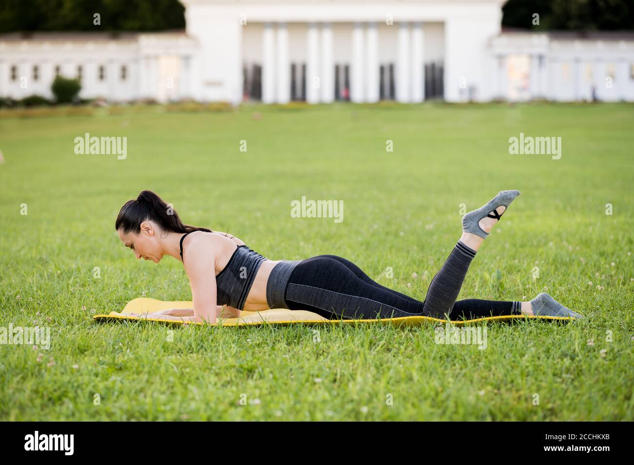 Schöne junge Frau auf einer gelben Matratze liegen, Pose, während das Tragen eines engen Sport-Outfit im Park tun Pilates oder Yoga, Single-Bein Kick Experte e Stockfoto