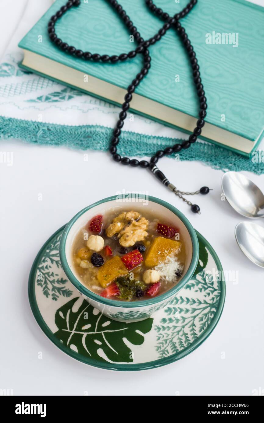 Religiöses Ritual "Ashura schnell" in Islam Zusammensetzung mit Ashura Gericht "Noah's Puding", heilige Buch Koran und Rosenkranz auf weiß. Stockfoto