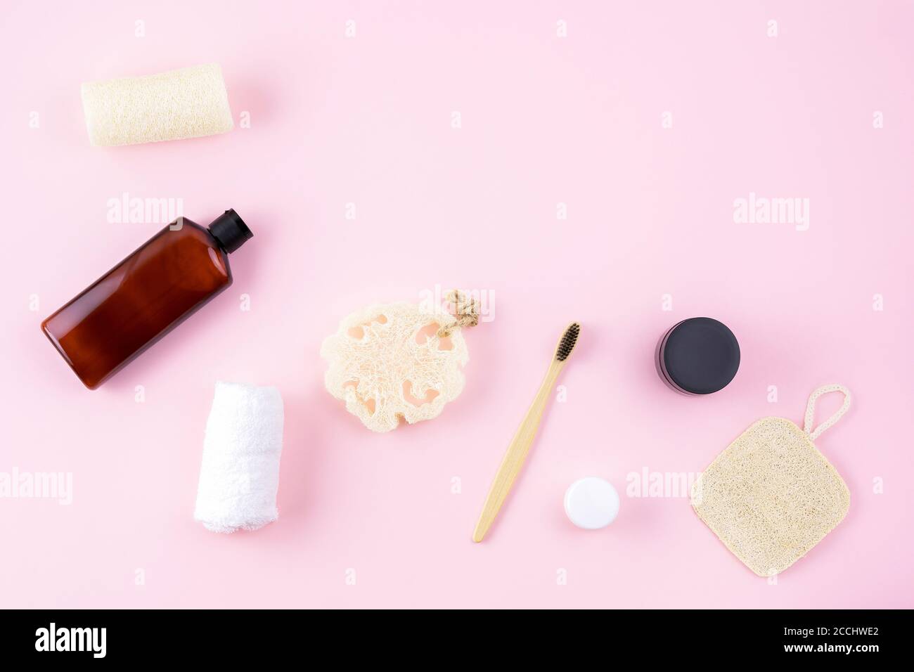 Massagegerät, Creme, Flasche, Loofah Schwamm Scheuerschwamm, Bambuszahnbürste auf rosa Oberfläche. Badezimmer Accessoire Zusammensetzung. Wellness keine Verschwendung Stockfoto