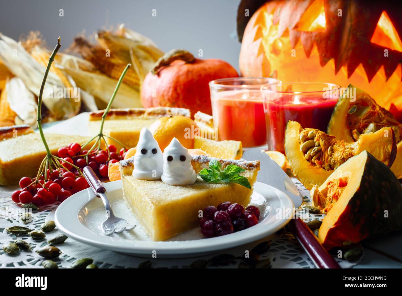 Süße hausgemachte halloween Kürbiskuchen mit Minzeblatt und kleinen Geistern auf weißem Teller Nahaufnahme. Kerzen und Jack-o-Laterne auf dem Hintergrund. Traditionelles Urlaubsessen Stockfoto