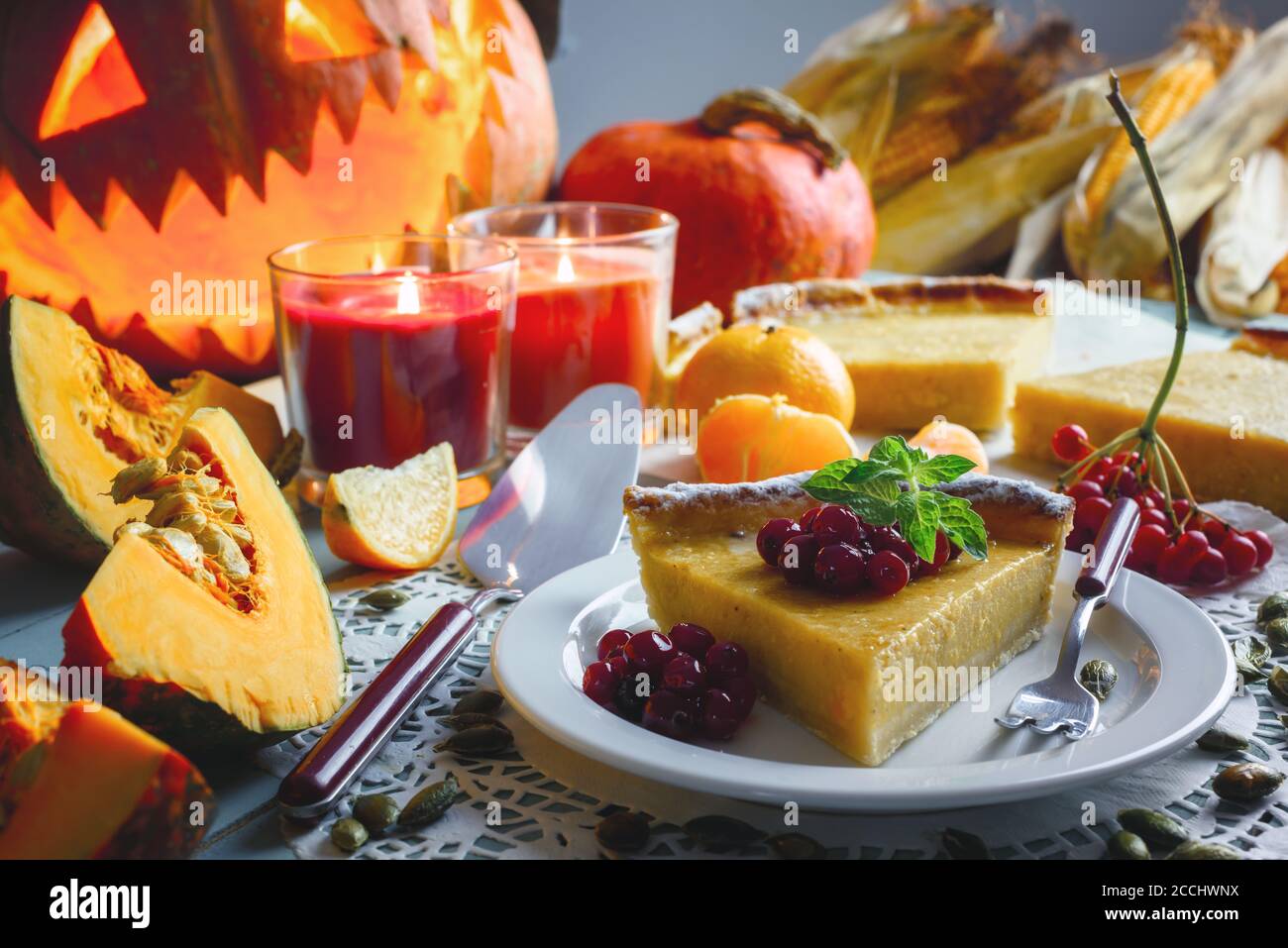 Köstliche süße hausgemachte halloween Kürbiskuchen mit Minzeblatt und Preiselbeermarmelade auf weißem Teller Nahaufnahme. Kerzen und Jack-o-Laterne auf dem Hintergrund. Traditionelles Urlaubsessen Stockfoto