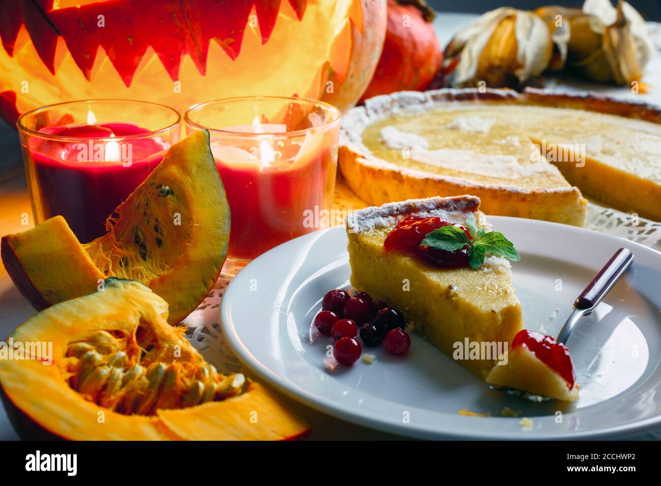 Stück süße hausgemachte halloween Kürbiskuchen mit Minzeblatt und Preiselbeermarmelade auf weißem Teller Nahaufnahme. Kerzen und Jack-o-Laterne auf dem Hintergrund. Traditionelles Urlaubsessen Stockfoto