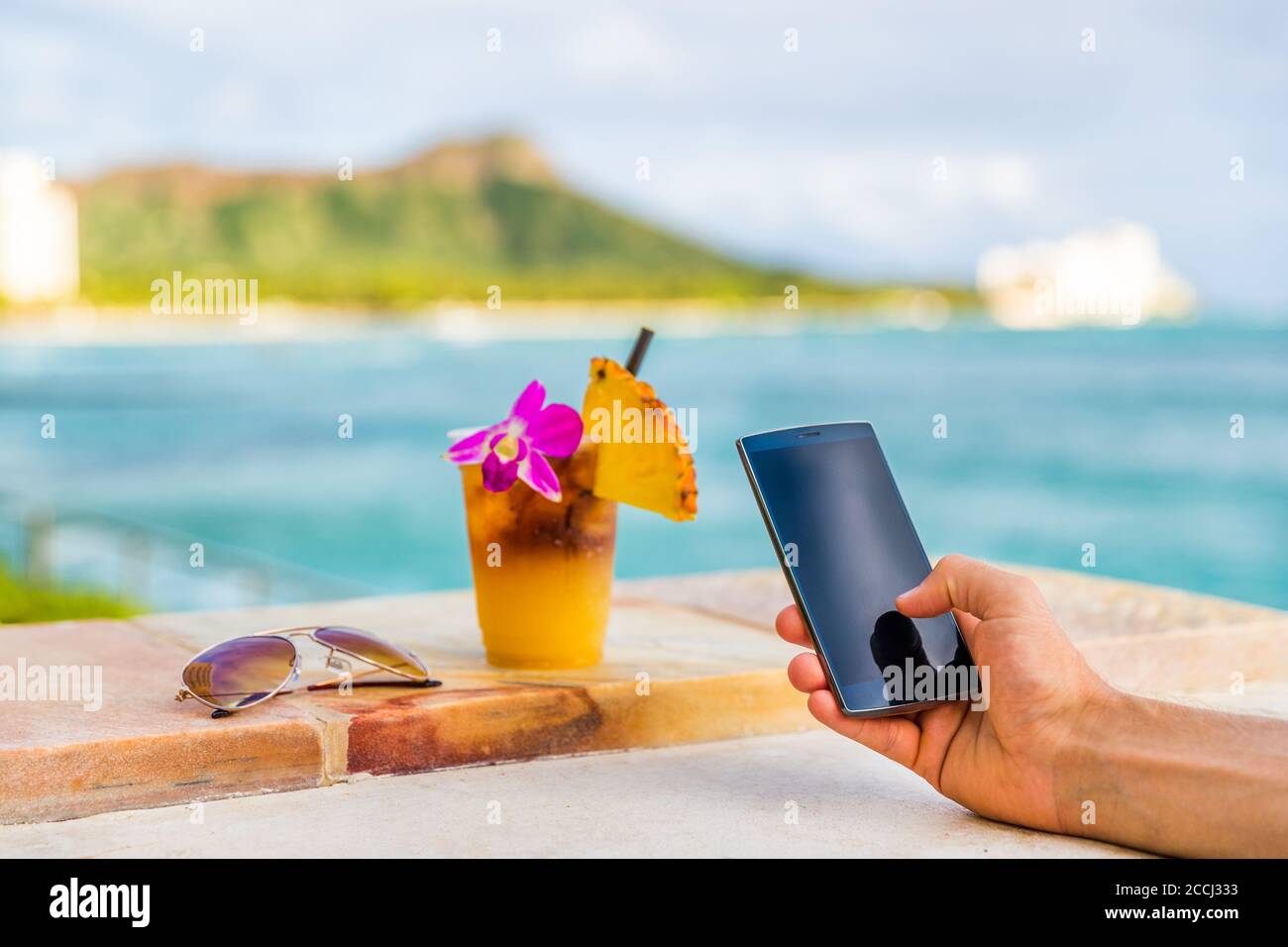 Handy-App Mann SMS-Aufnahme Handy-Bild von Hawaii Mai Tai Drink Cocktail an Hawaii Beach Bar. Glas mit Blume, Ananas, Sonnenbrille Stockfoto