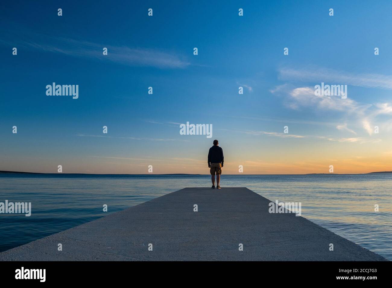 Mann, der auf einem langen Dock steht und den Horizont des Meeres bei Sonnenuntergang, Insel von Pag, Adria, Kroatien, Gedanken-Konzept beobachtet Stockfoto
