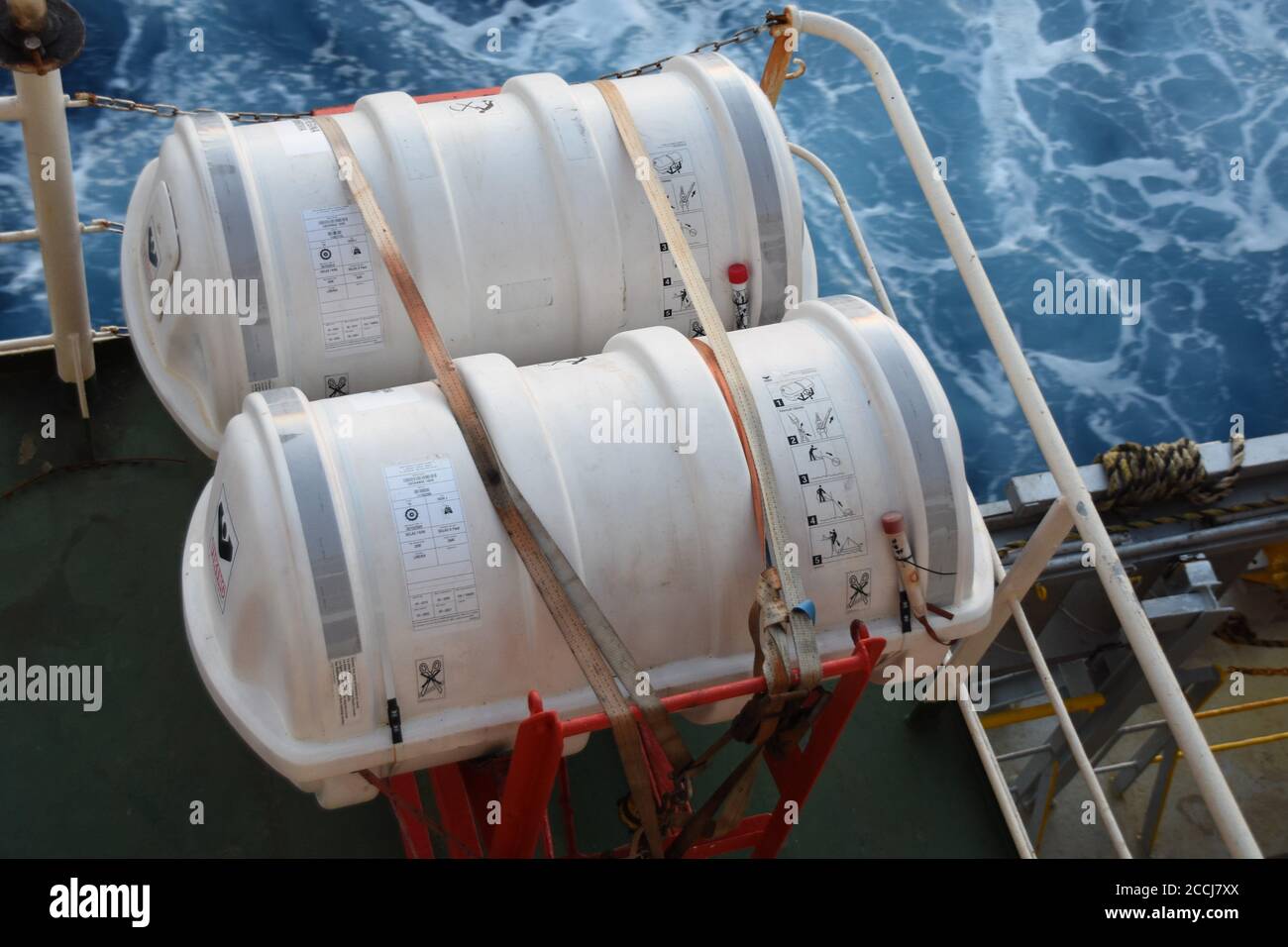 Zwei Liferafts, die mit weißen Bändern in der roten Wiege auf dem Frachtschiff von der rechten Seite des Aufbaus gesichert sind. Stockfoto