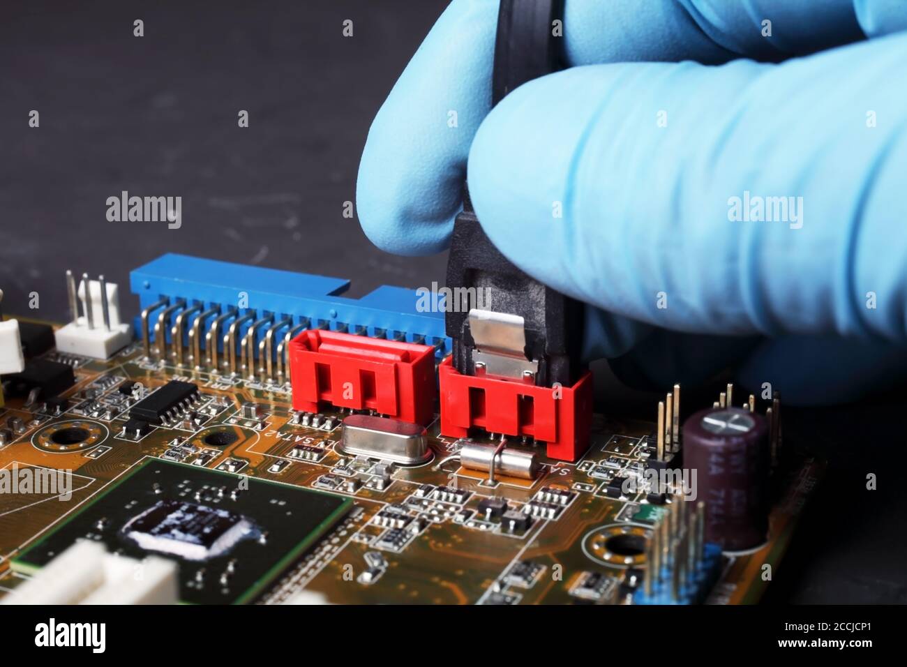 Serielle ATA-Verbindung des Kabels mit Computer-Motherboard, Hand des Ingenieurs mit blauem Handschuh, selektiver Fokus Stockfoto