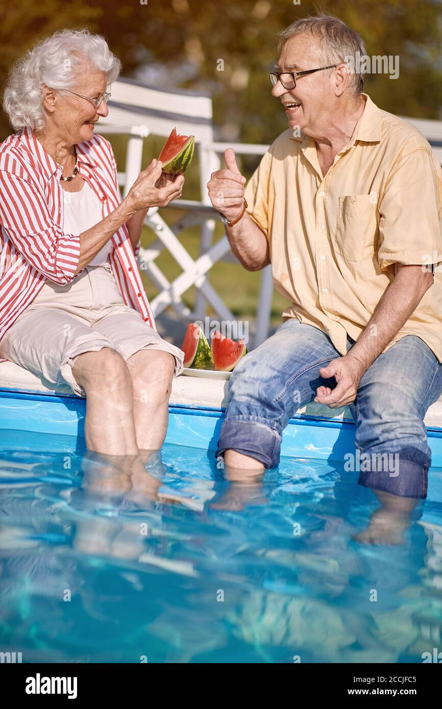Romantische glückliche ältere Mann und Frau genießen im Sommerurlaub in der Nähe von Schwimmbad und essen Wassermelone. Stockfoto