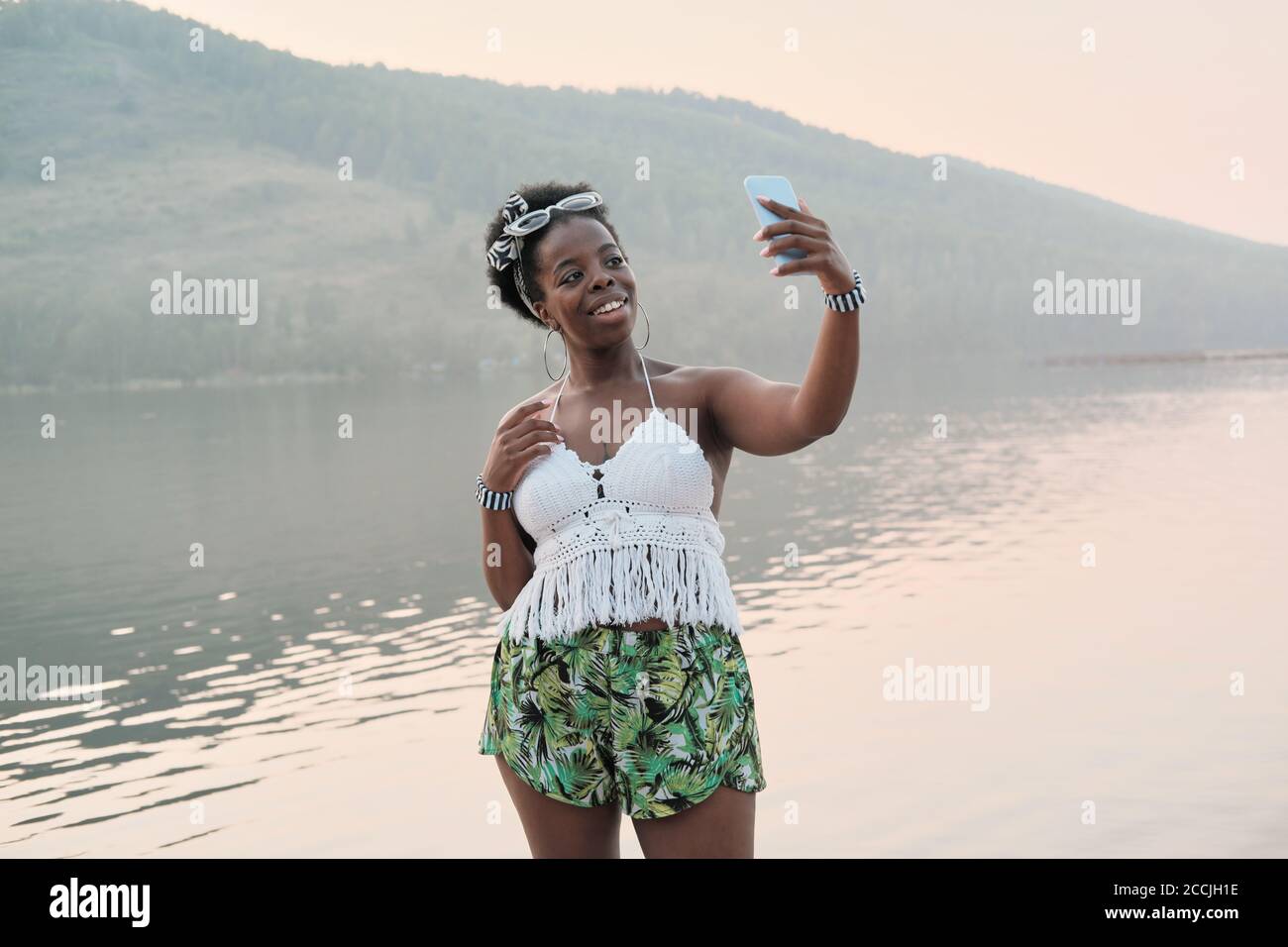 Afrikanische junge Frau, die gegen den Berg und den See steht Und Selfie auf ihrem Handy machen Stockfoto