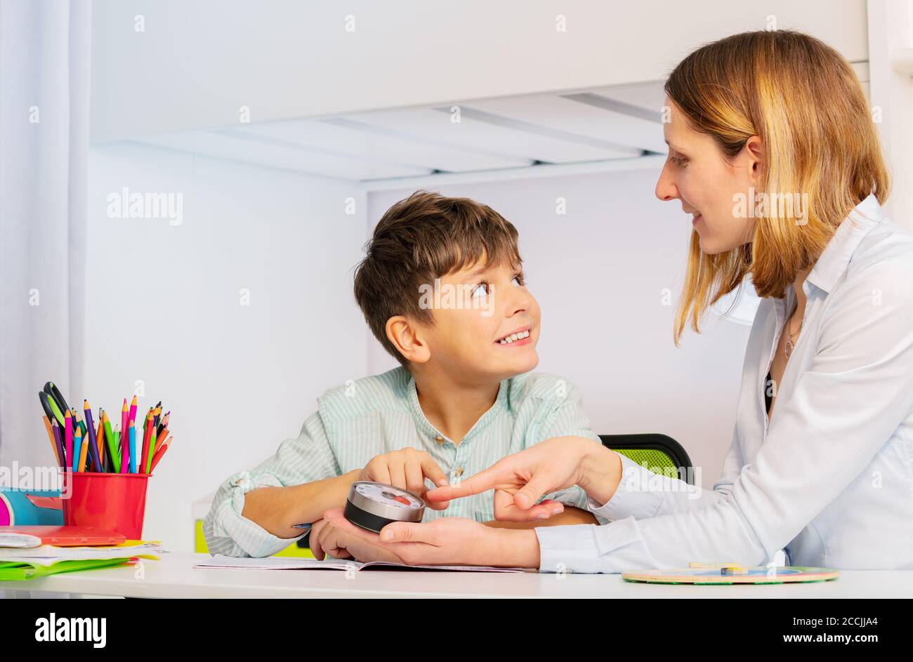 Autistischer Junge während der ABA-Therapie Blick auf Lehrer zeigt auf Stundenzähler Lernen, um Klassenverfahren zu erlernen und Zeit zu verstehen Konzept Stockfoto