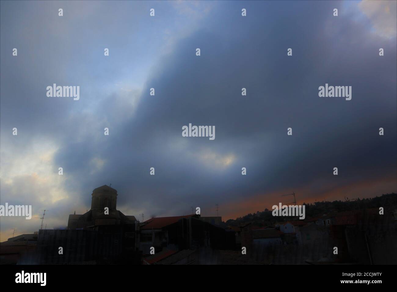 Silhouette eines dunklen Kirchturms und eines Hügels gegen die Sturmwolken. Mystische Wolken auf grauem Himmel Stockfoto
