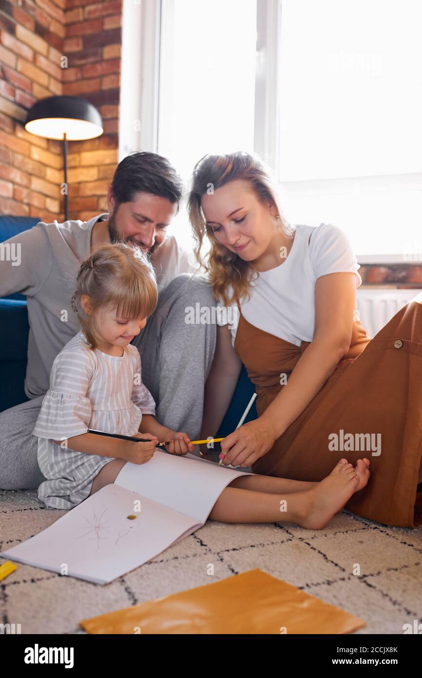 Freundliche Familie Liebe Spedning Zeit mit Tochter zu Hause, junge Eltern sitzen mit Mädchen auf dem Boden, sie ist malen, Zeichnung Stockfoto