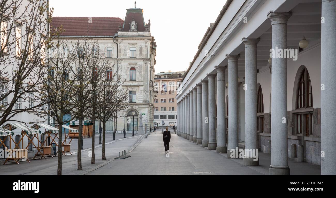 Rückansicht einer nicht erkennbaren Frau, die während einer Corona-Virus-Pandemie im leeren, mittelalterlichen Stadtzentrum von Ljubljana unterwegs ist. Fast keine Leute draußen auf Stockfoto