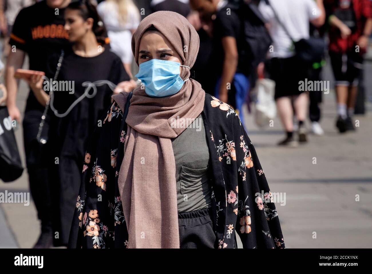 Junge muslimische Frau, die ein operatives Gesicht trägt, in einer belebten Straße, London, Großbritannien. Stockfoto