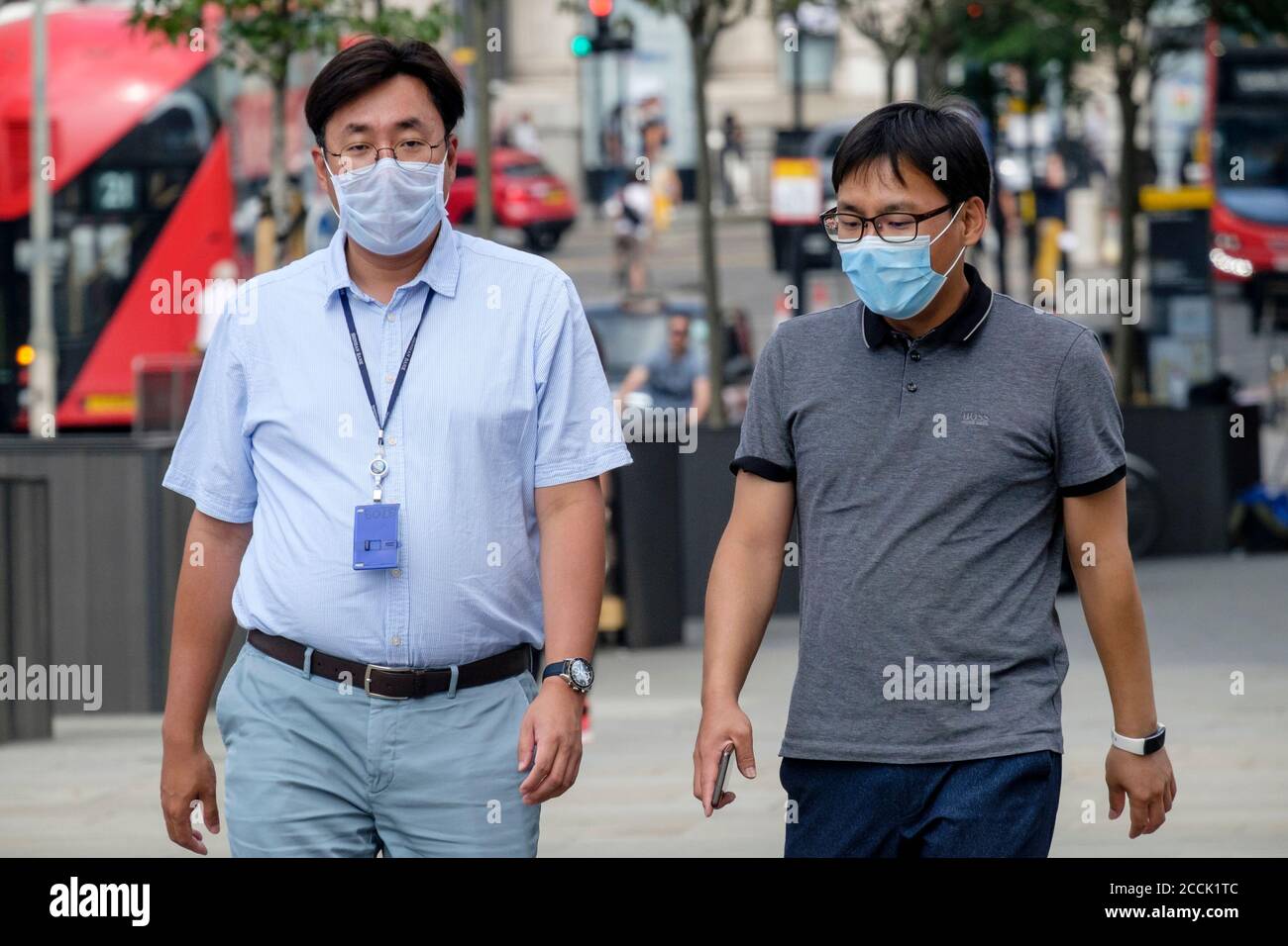 Zwei ethnische chinesische Männer, die mit chirurgischen Gesichtsmasken auf der Straße spazieren, London, Großbritannien Stockfoto