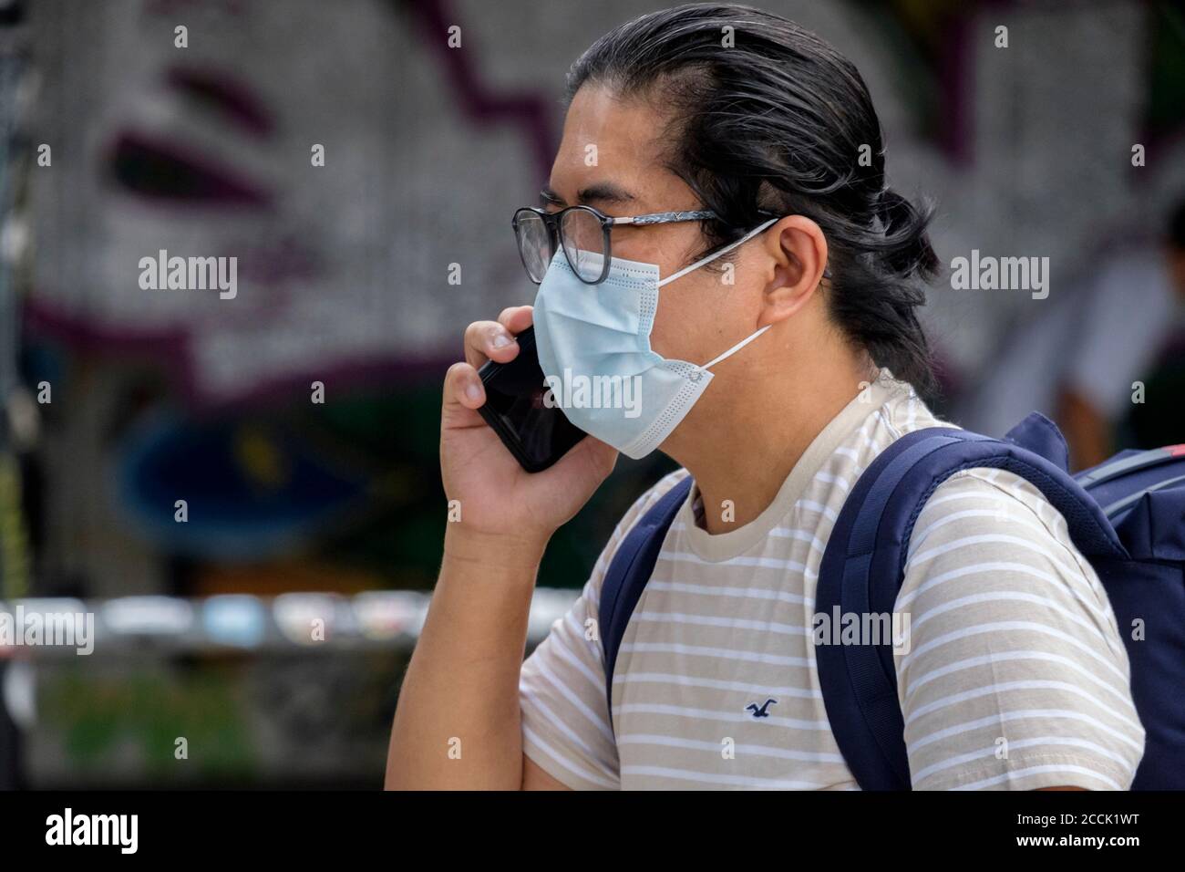 Junger Mann spricht auf dem Handy, während er eine chirurgische Gesichtsmaske in der Straße, London, trägt. VEREINIGTES KÖNIGREICH. Stockfoto