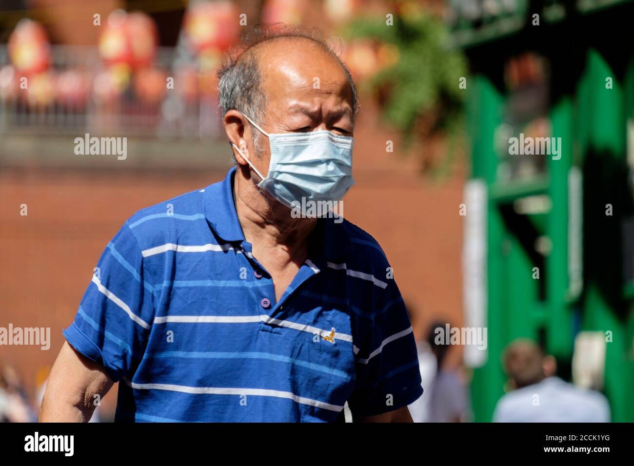 Älterer Chinese, der auf der Straße mit chirurgischen Gesichtsmasken geht, London, Großbritannien Stockfoto