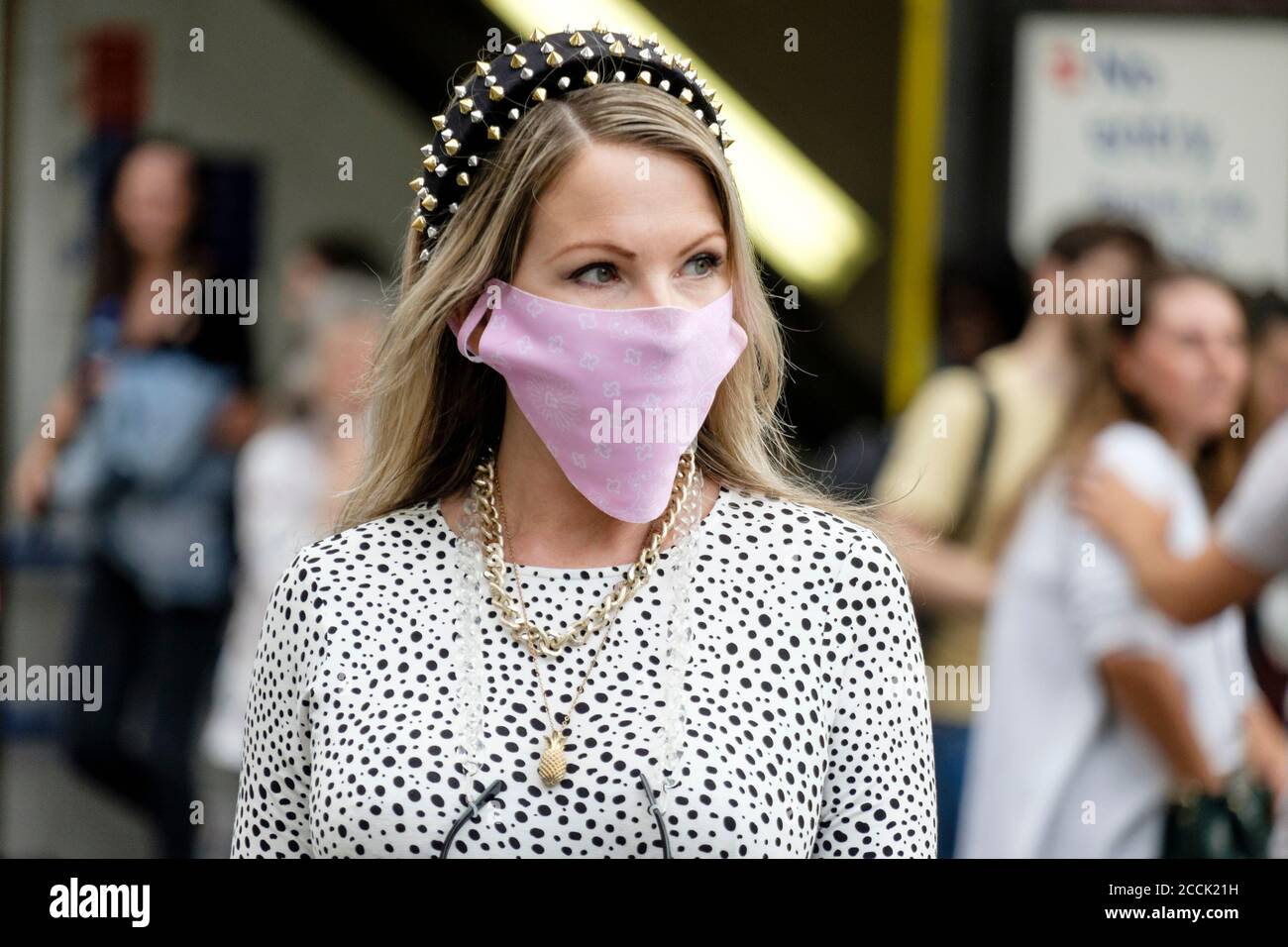 Elegant gekleidete junge Frau mit Designer-Gesichtsbedeckung auf belebten Straße, London, Großbritannien Stockfoto