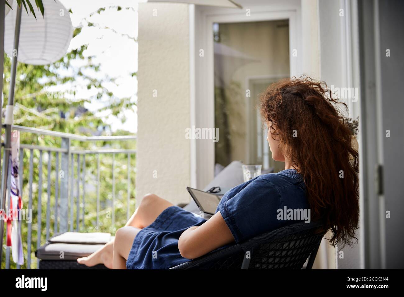 Frau liest aus E-Reader, während sie auf einem Stuhl auf dem Balkon sitzt Stockfoto