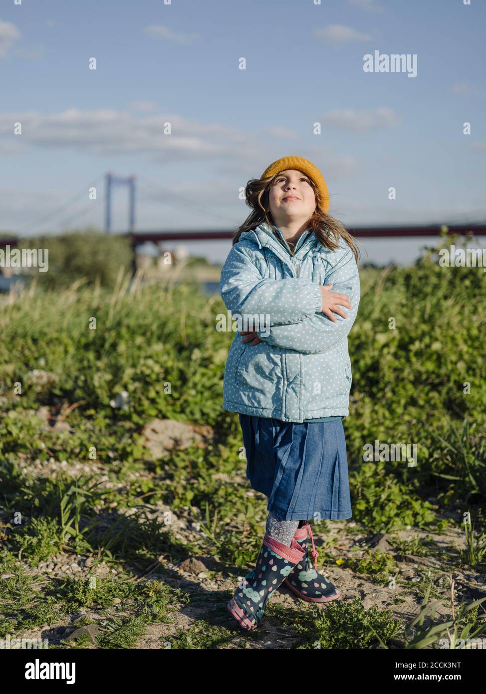 Nettes Mädchen mit gekreuzten Armen stehen auf dem Land gegen den Himmel An sonnigen Tagen Stockfoto