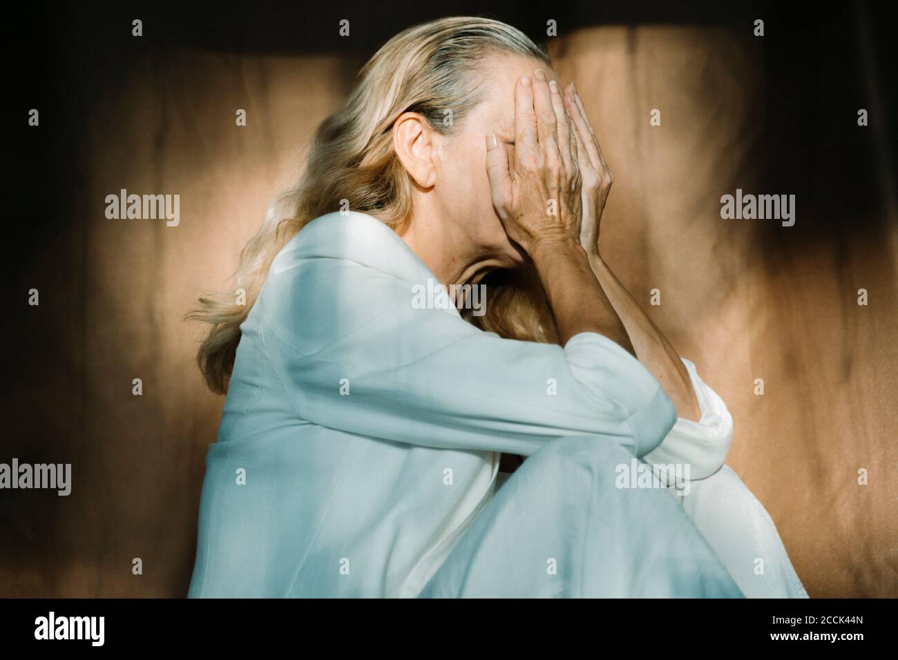 Traurige ältere Frau, die allein sitzt und das Gesicht mit den Händen bedeckt Stockfoto