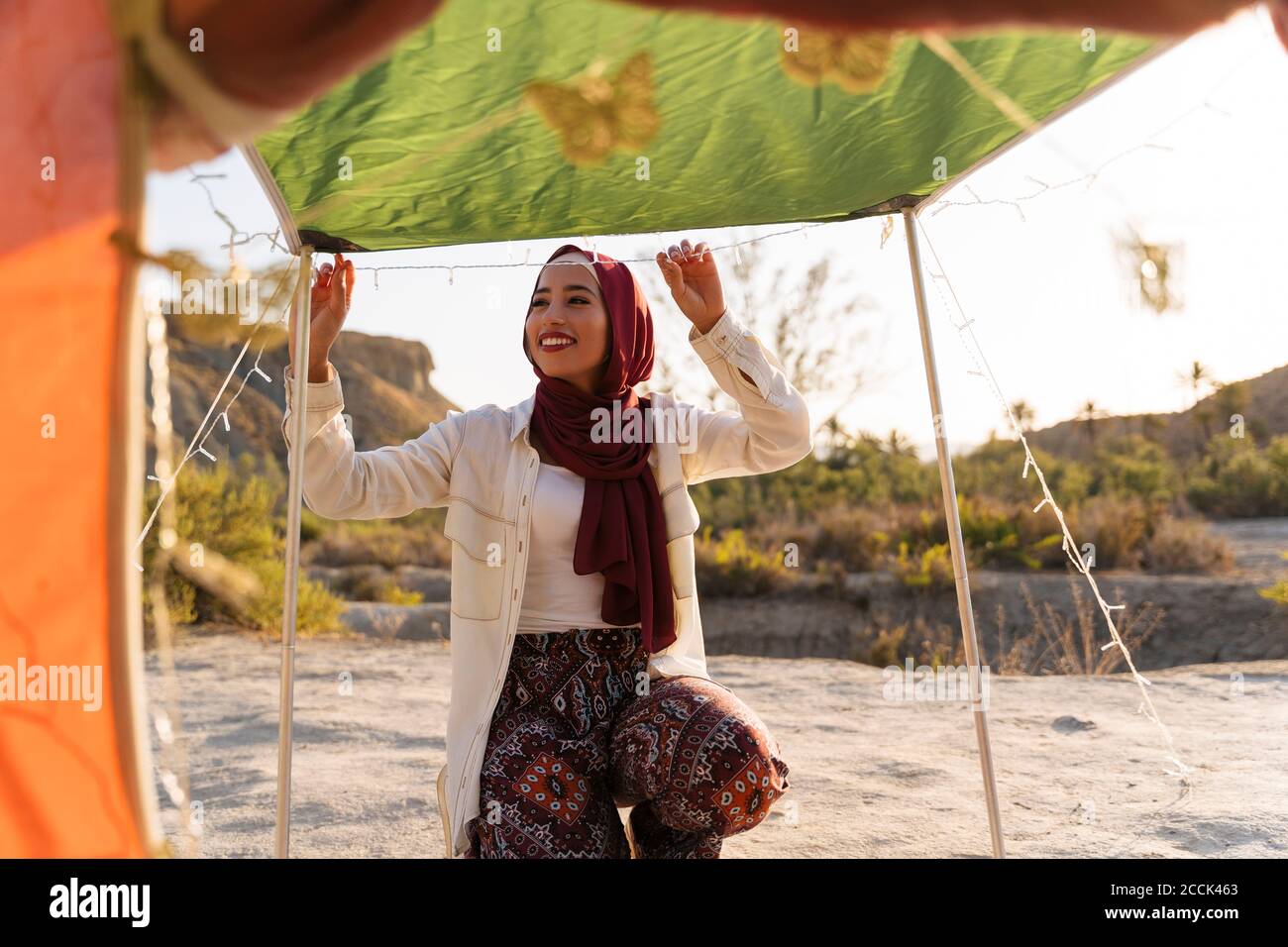 Lächelnde junge Touristenfrau in Hijab, die ein Zelt schmückt Stockfoto