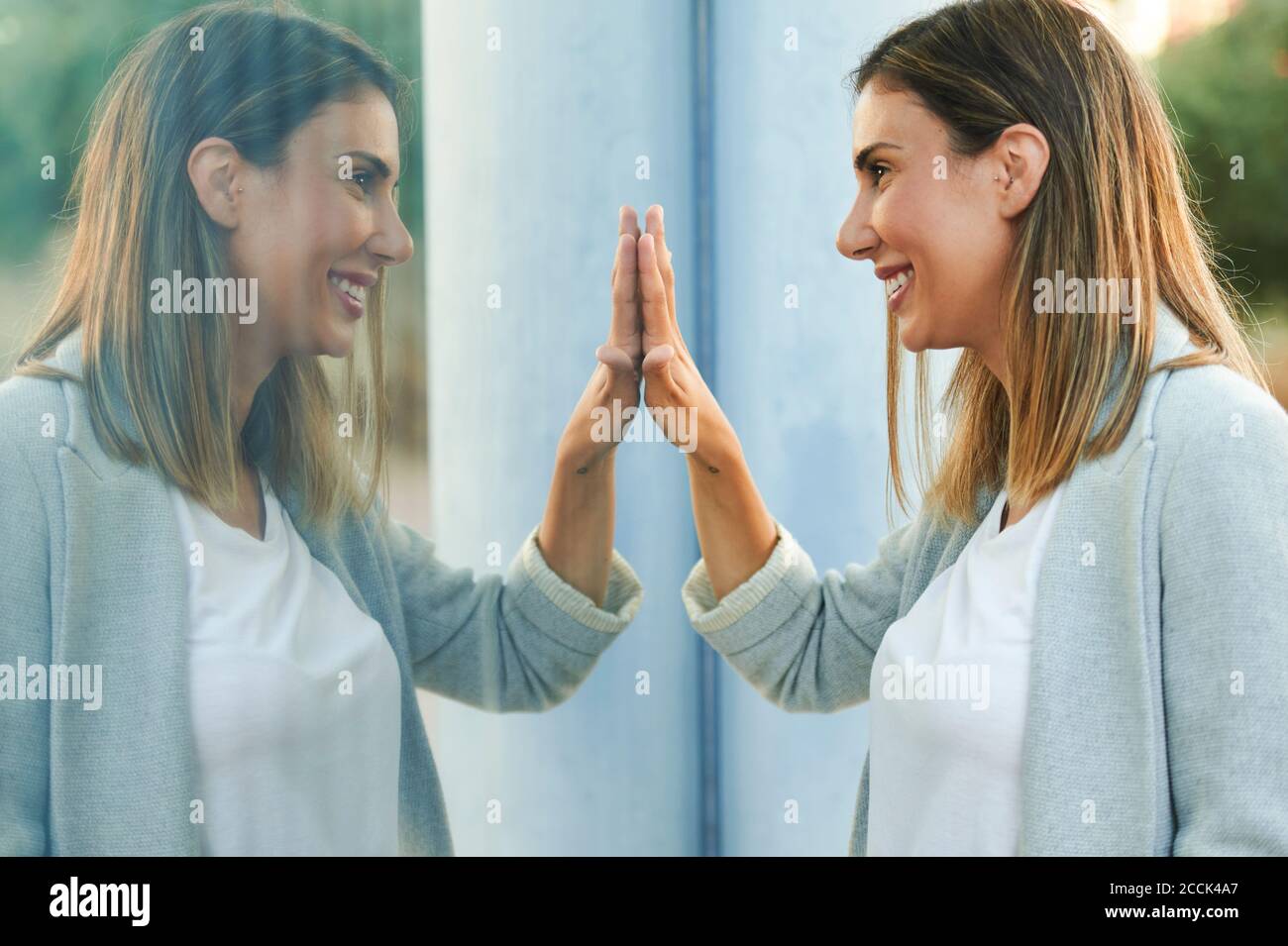 Symmetrisches Bild der lächelnden Geschäftsfrau berühren Fensterglas Stockfoto