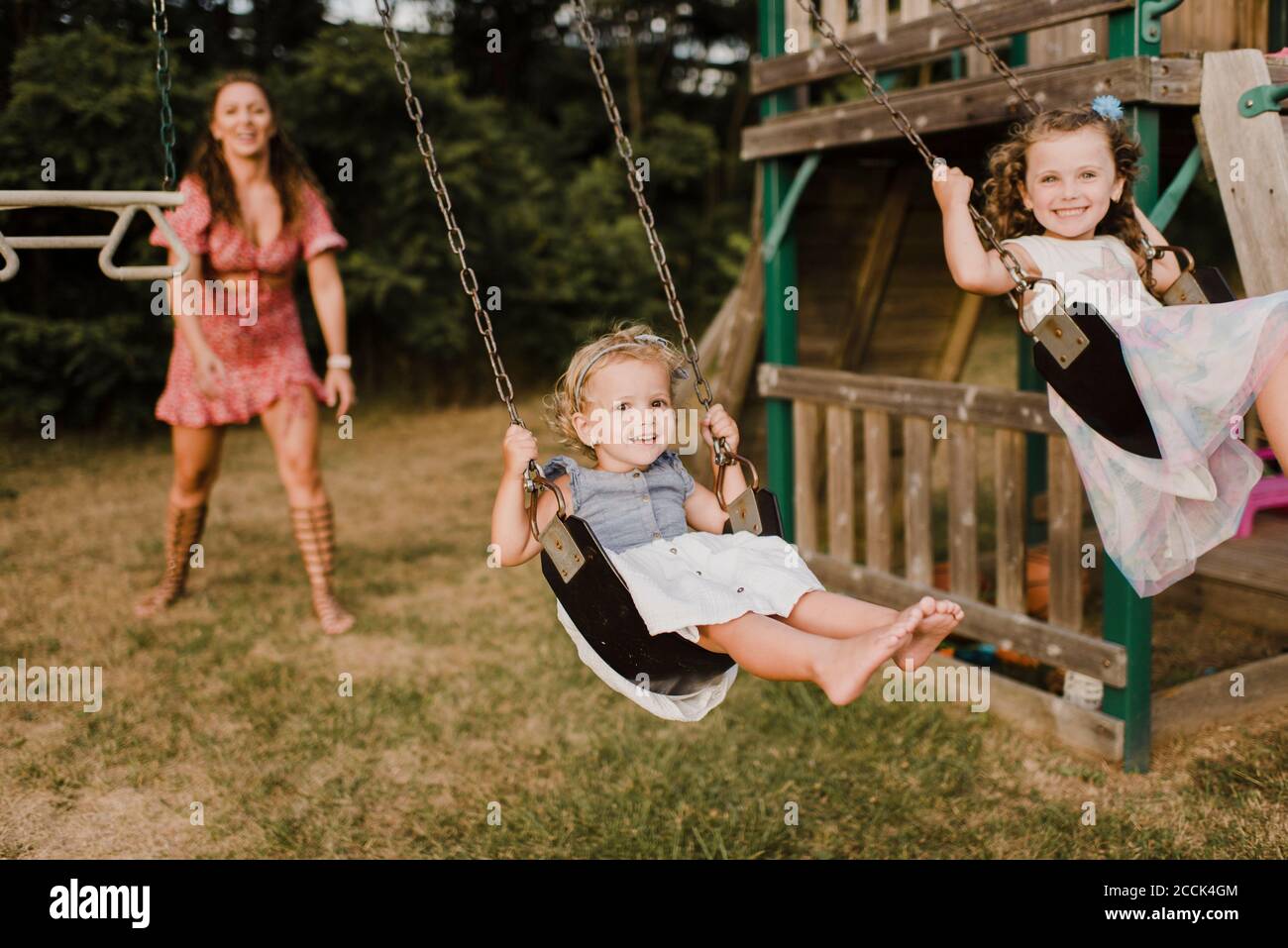 Glückliche Mädchen auf einer Schaukel mit Mutter im Hintergrund Stockfoto